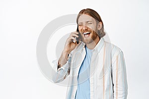 Portrait of handsome happy guy talking on cellphone, laughing and smiling during phone call, standing in casual outfit