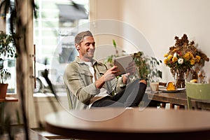 Portrait of handsome happy guy, young man sits in cafe, watching videos on digital tablet, wearing wireless headphones