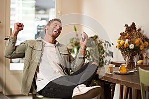 Portrait of handsome happy man in cafe, listens to music in wireless earphones, holding smartphone, connects to public