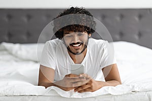 Portrait of handsome hindu guy laying on bed with phone