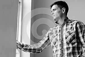 Portrait of handsome hipster man by the window indoors in black and white