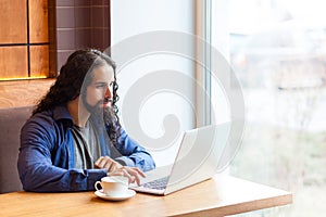 Portrait of handsome intelligence bearded young adult man freelancer in casual style sitting in cafe and searching information for