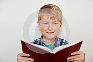 A portrait of handsome little boy with fair hair and blue eyes holding a book in his hands while standing over white background ha