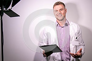 Portrait of handsome male doctor, smiling and looking at camera with behind the scenes studio lamp in shot