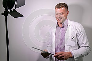 Portrait of handsome male doctor, smiling and looking at camera with behind the scenes studio lamp in shot