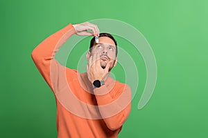 Portrait of handsome man applying eyedropper to treat irritation while standing on green background