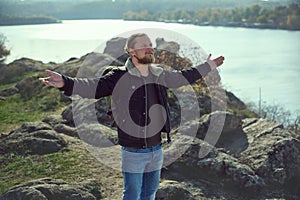 Portrait of handsome man with arms wide open enjoying the lake view. Redhead bearded man with arms outstretched enjoying the