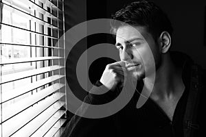 Portrait of handsome man with beard sitting next to window with blinds