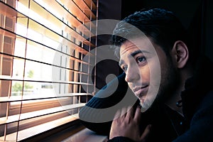 Portrait of handsome man with beard sitting next to window with blinds