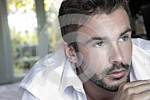 Portrait of handsome man with blue eyes, beard and open white shirt looking off camera