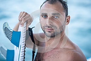Portrait of handsome man with blue eyes, surfer holding surf board with blue fins and blue ocean