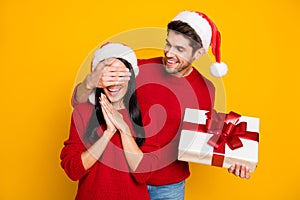 Portrait of handsome man with brown hair hide his excited wife eyes give her package wear red pullover isolated over