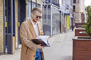 Portrait of a handsome man, businessman, scientist or teacher. He walks along a modern city street with a folder of documents