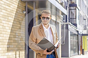 Portrait of a handsome man, businessman, scientist or teacher. He walks along a modern city street with a folder of documents and