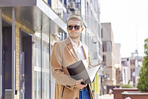 Portrait of a handsome man, businessman, scientist or teacher. He walks along a modern city street with a folder of documents