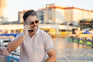 Portrait of handsome man chatting on phone outdoor. Stylish man talking on phone dressed in polo. Fashion male posing on