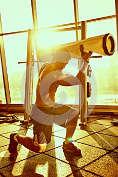 Portrait of a handsome man doing push ups exercise with modern weight equipment in rays of sunlight in fitness gym.