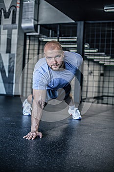 Portrait of a handsome man doing push ups exercise with one hand in fitness gym. dressed in a sports uniform