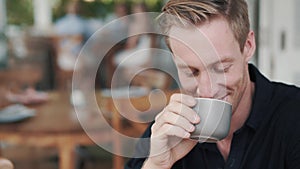 Portrait of handsome man drinking hot beverage from cup in cafe and smiling