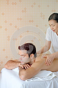 Portrait of handsome man enjoy with Thai masseuse massage to him and he lie on bed in spa room with day light