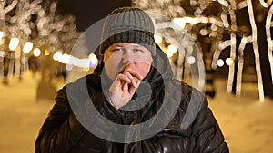 Portrait of handsome man gesturing for silence with finger outdoors during cold winter night