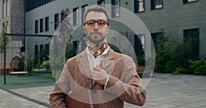 Portrait of handsome man in glasses adjusting jacket while looking to camera. Bearded man in neckwear and suit holding