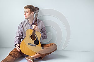 Portrait of handsome man with guitar siting on floor in studio