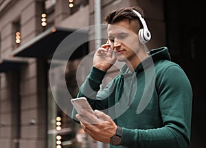 Portrait of handsome man with headphones and smartphone listening to music on city street