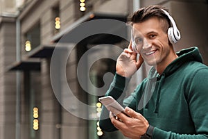 Portrait of handsome man with headphones and smartphone listening to music on street. Space for text