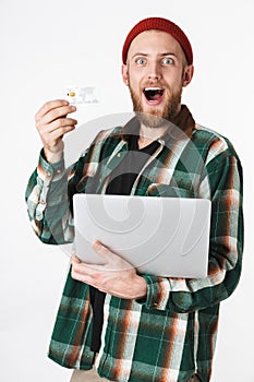 Portrait of handsome man holding silver laptop and credit card, while standing isolated over white background
