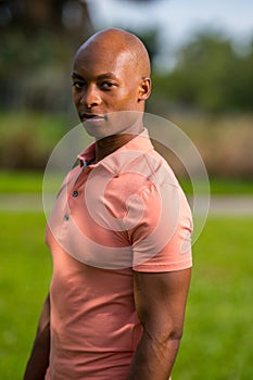 Portrait handsome man looking over shoulder towards camera. ADult bald male model posing in a pink polo style shirt