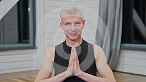 Portrait of handsome man in namaste pose holding hands while enjoying spiritual meditation in apartment