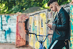 Portrait of handsome man with phone in hand, casually dressed against graffiti painted wall. Stylish european man