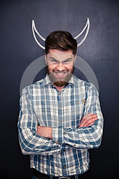 Portrait of handsome man pretending devil standing over chalkboard background