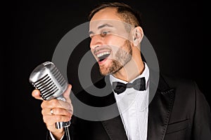 Portrait of handsome man sing on microphone on black background.