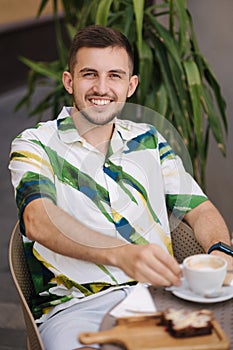 Portrait of handsome man sitting in cafe and drinking cappuccino. Young man