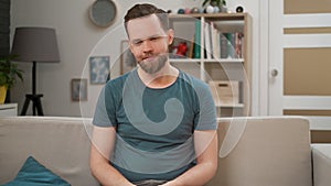 Portrait of a handsome man sitting on a couch at living room, looking at camera. Young man smile happily and sit on sofa