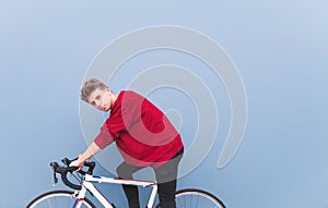 Portrait of handsome man sitting on white bicycle on a background of blue wall and looking at the camera