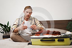 Portrait of handsome man, tourist, looking at his holiday tickets, booked vacation with travel agency, sitting on bed