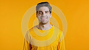 Portrait of handsome man in yellow t-shirt winking with eye, flirting and smiling to camera. Guy in studio on bright