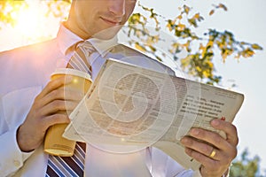 Portrait of handsome mature businessman holding cup of coffee while reading newspaper in park during break