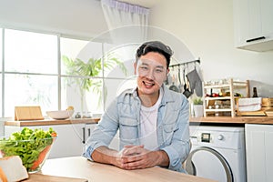 Portrait of handsome mature male smile and look at camera in kitchen. Attractive young man sitting on table feel happy and enjoy