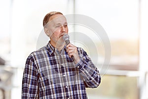 Portrait of a handsome mature man is singing standing indoors.