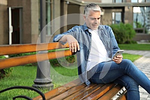 Portrait of handsome mature man using mobile phone in city
