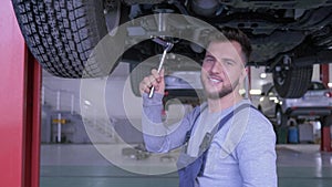 Portrait of handsome mechanic in boilersuit on service station works with a key under the bottom of car