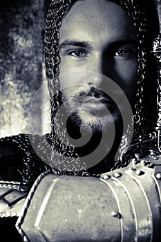 Portrait of handsome medieval knight in suit of armour with beard and blue eyes looking at camera