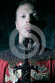 Portrait of handsome medieval knight in suit of armour with beard looking seriously at camera