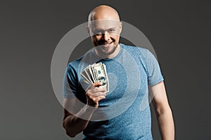 Portrait of handsome middle-aged man in grey shirt holding money over dark background.