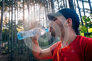 Portrait of a handsome mountain biker drinking water while wearing his baseball cap hat