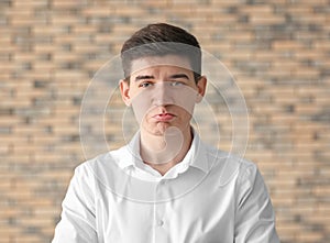 Portrait of handsome offended young man against brick wall